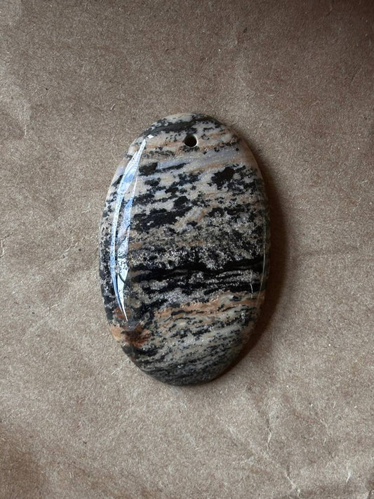 An oval dendritic jasper cabochon on brown paper background