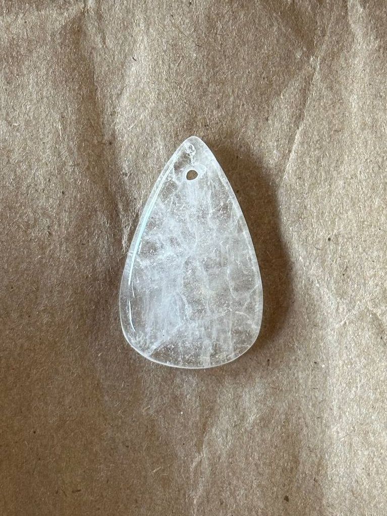 A teardrop-shaped clear quartz gemstone pendant with natural inclusions, resting on a textured brown kraft paper background.