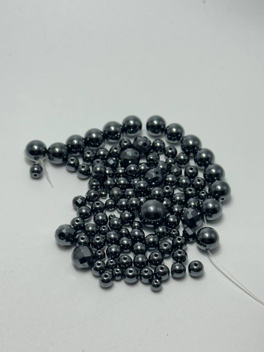 A small pile of black hematite round beads on white surface