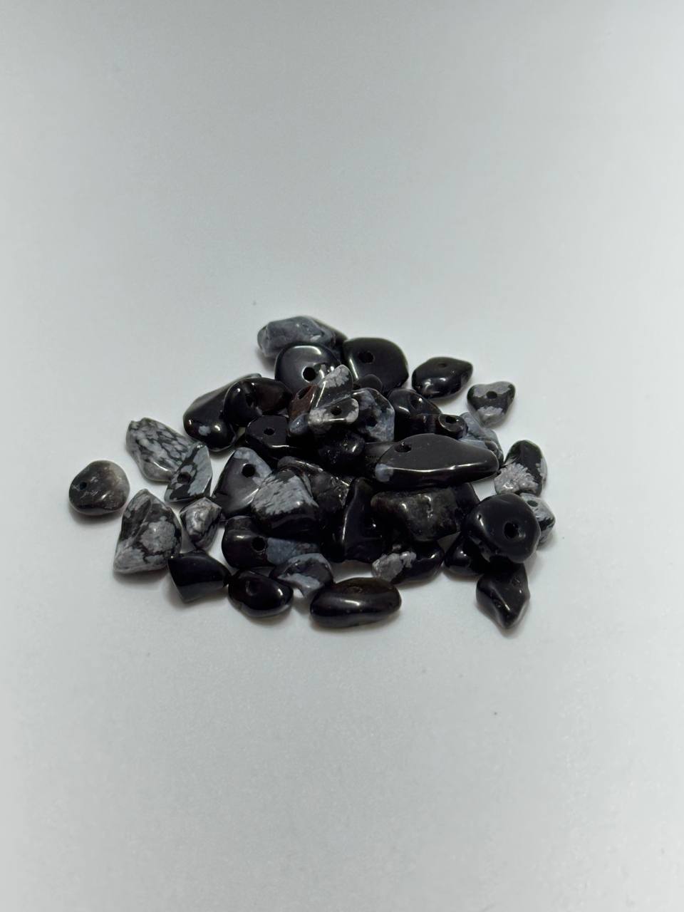 A small pile of polished black and gray stone chips or tumbled stones on a plain light background.