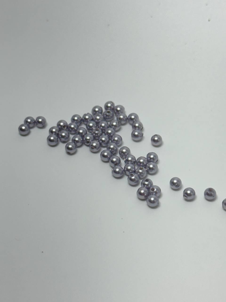 A small pile of 3mm crystal pearl beads in lavender on white surface