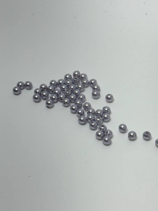A small pile of 3mm crystal pearl beads in lavender on white surface