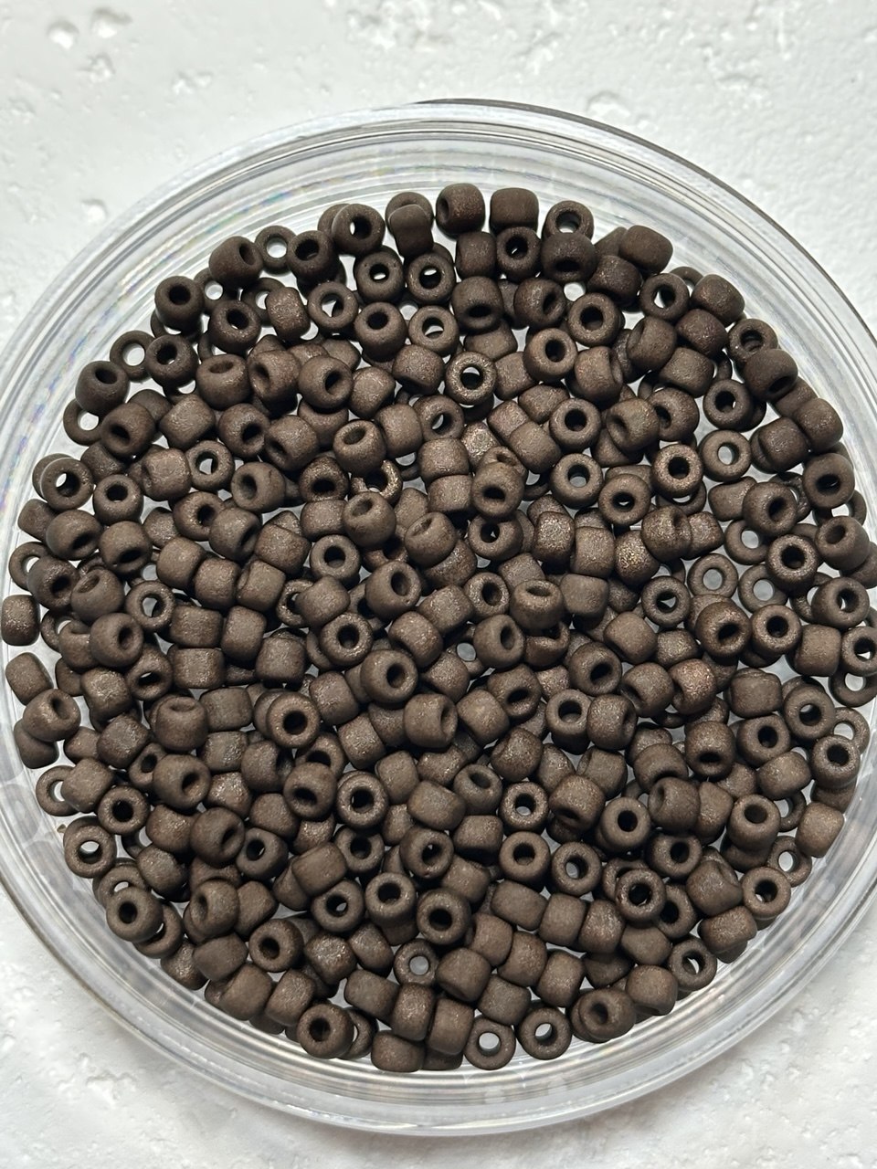 A small pile of toho size 6 metallic chocolate brown seed beads on white surface