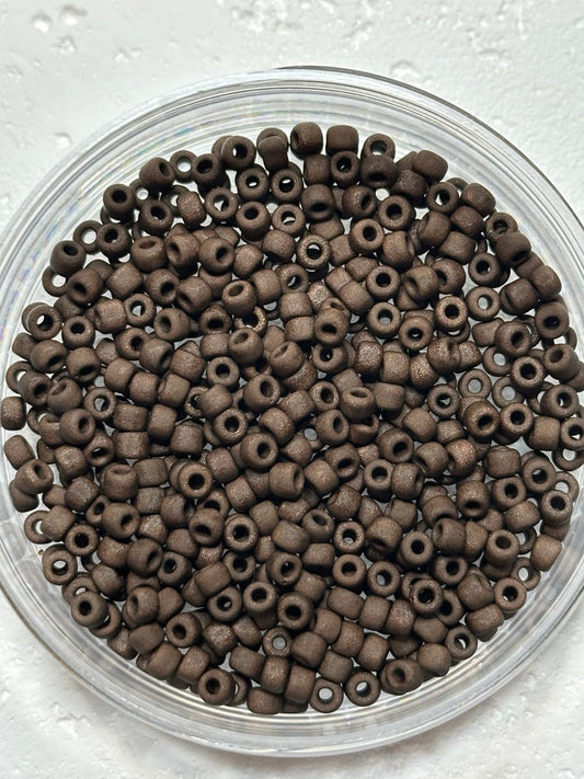A small pile of toho size 6 metallic chocolate brown seed beads on white surface