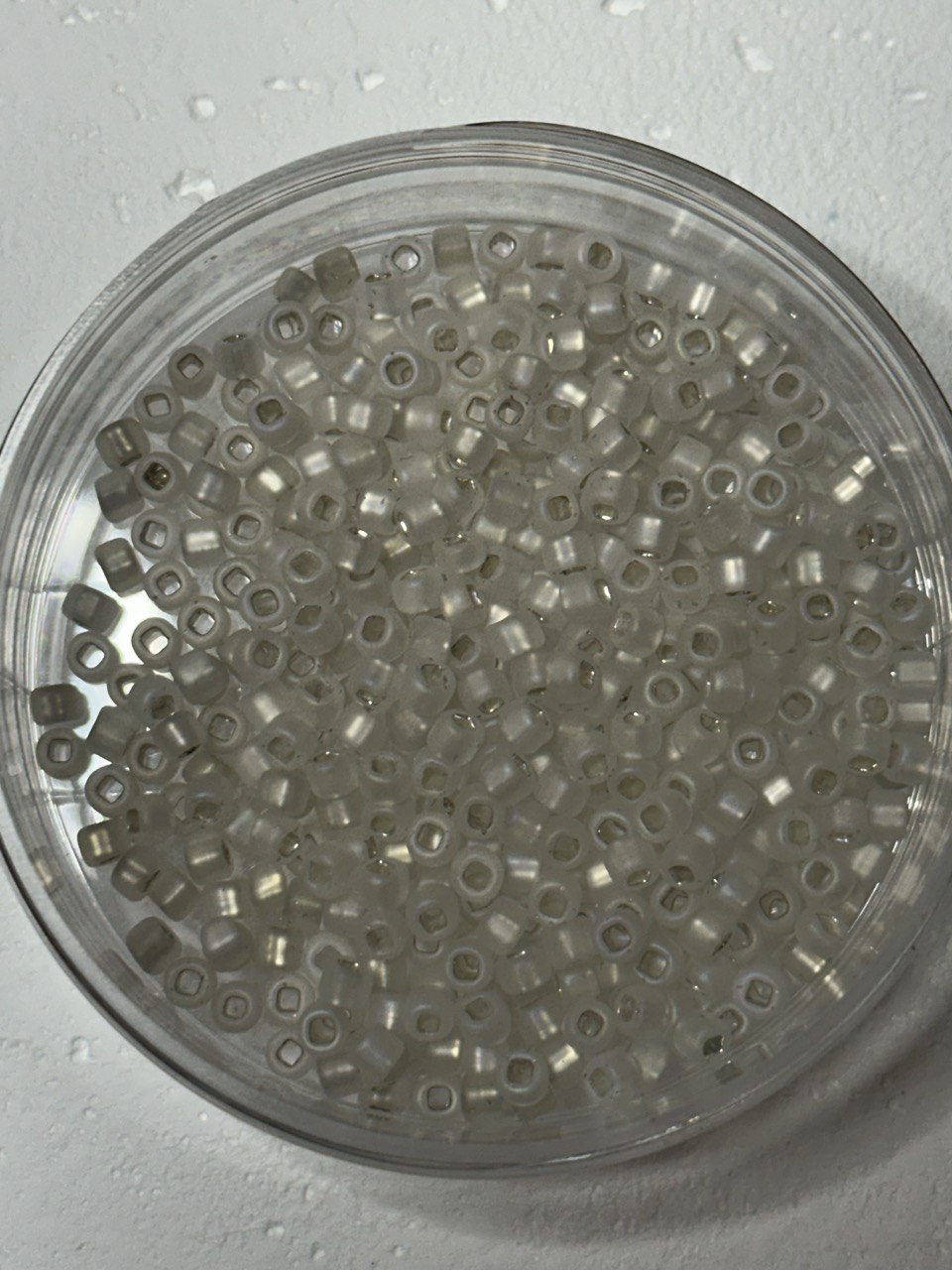 A small pile of matsuno round beads in white crystal matte AB with square holes on white surface