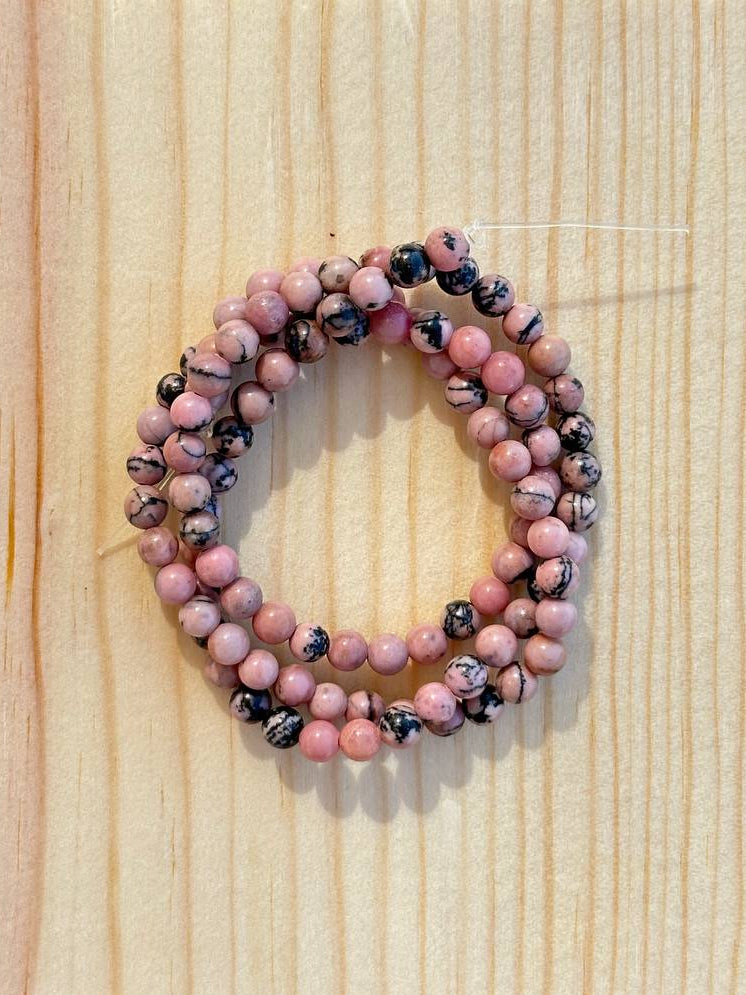 Stack of pink and black rhodonite beads on a wooden surface