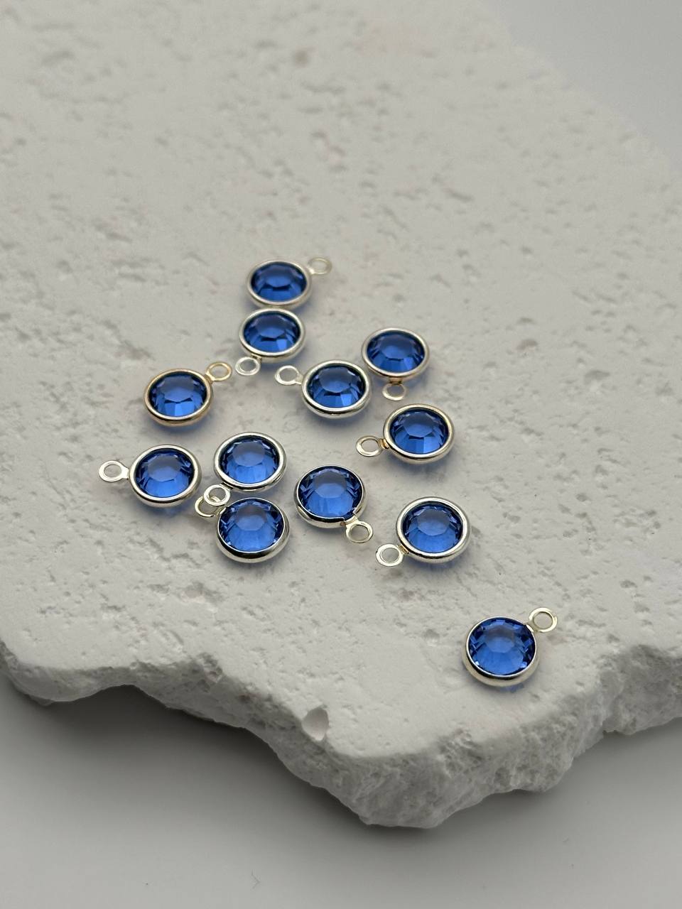 Blue gemstone connectors with silver prongs on a textured stone surface