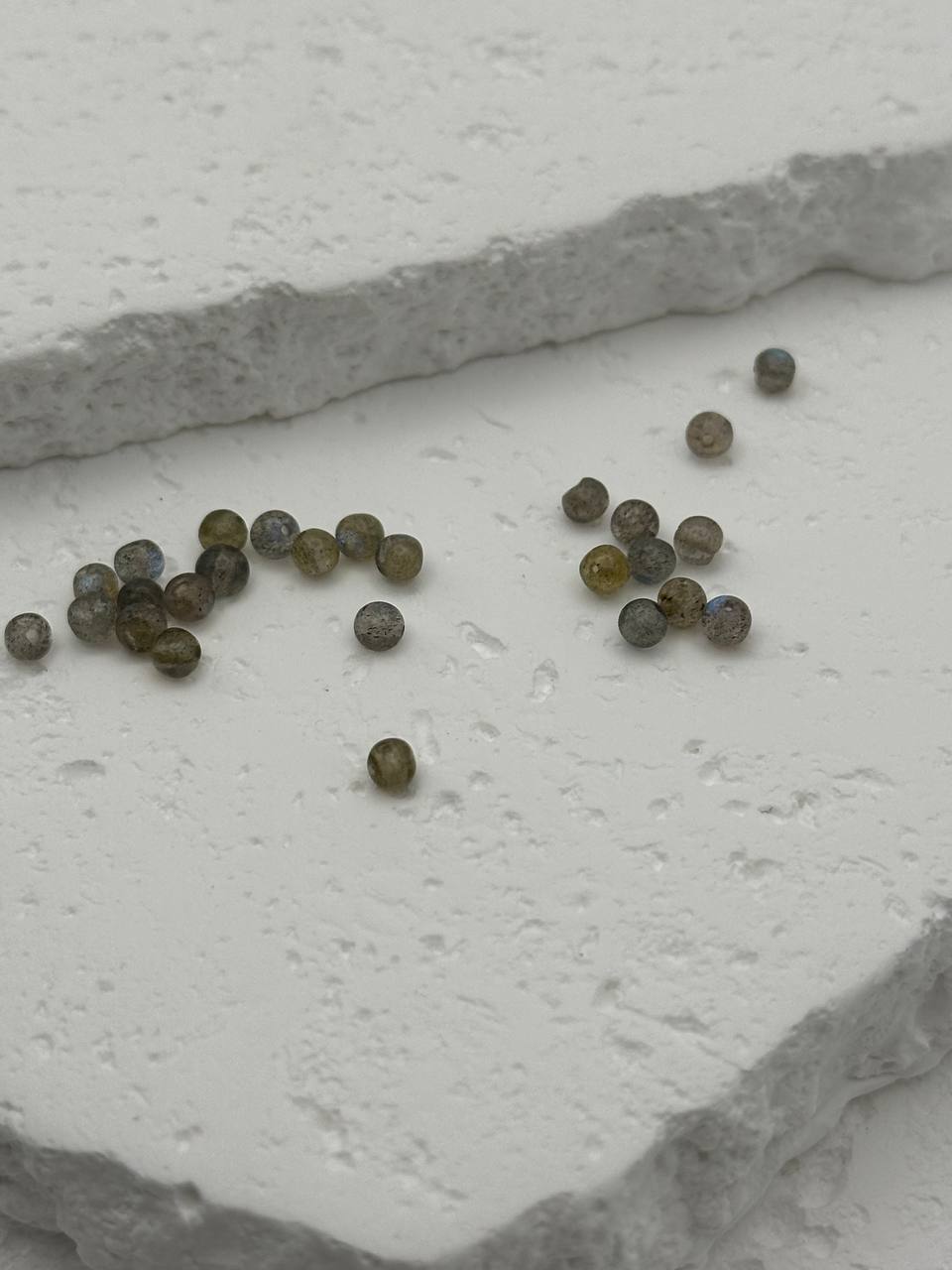 Small labradorite beads scattered on a textured white surface
