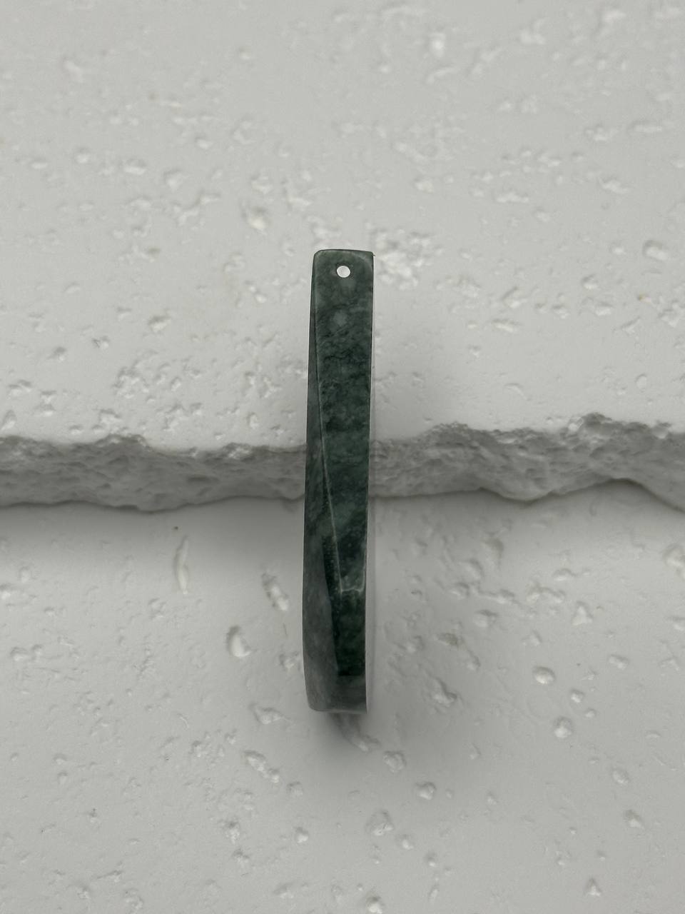 Green stone pendant on a gray surface