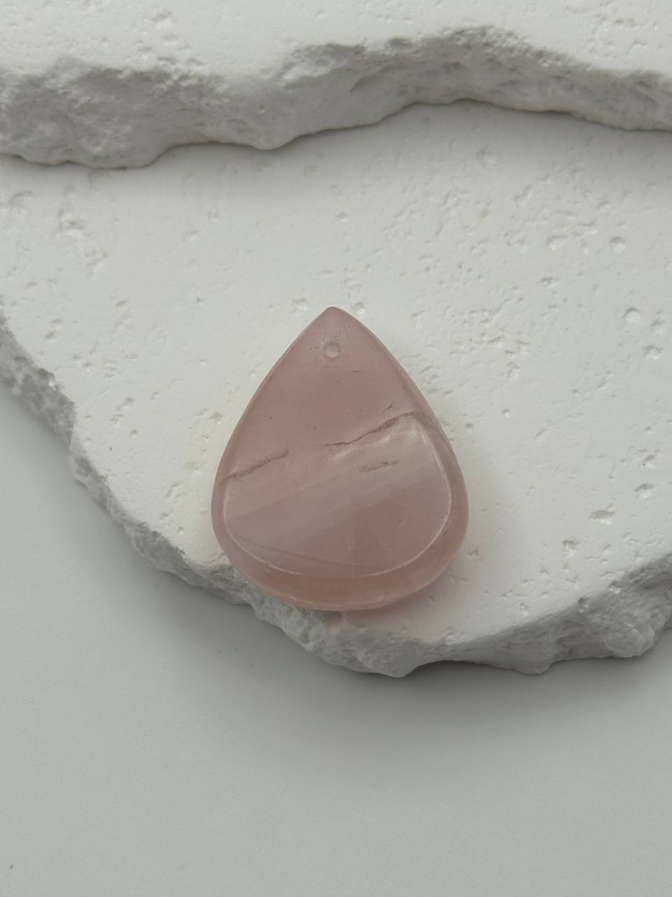 Teardrop-shaped pink stone on a textured white surface