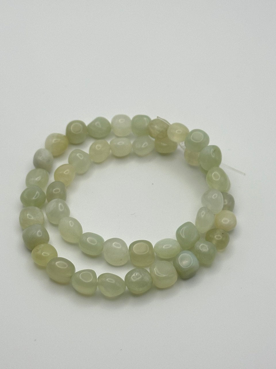 A string of light green serpentine nugget beads on a white surface