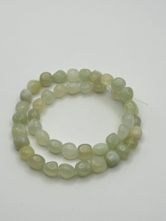 A string of light green serpentine nugget beads on a white surface