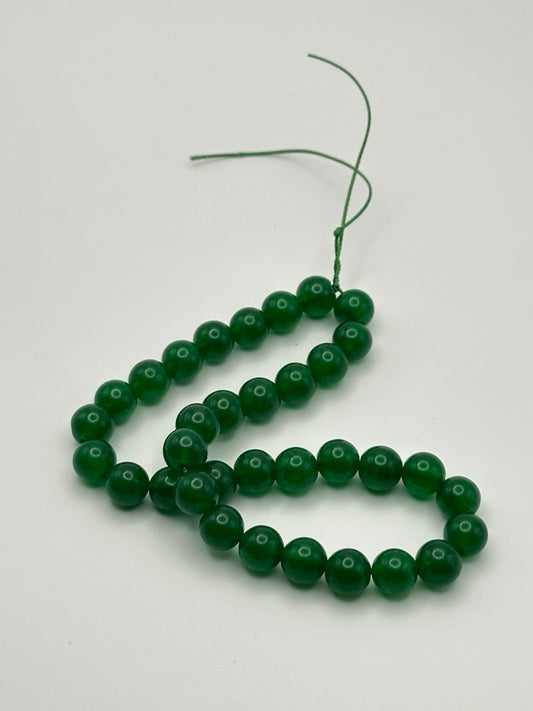 A string of bright green ching hai jade round smooth beads on a white surface