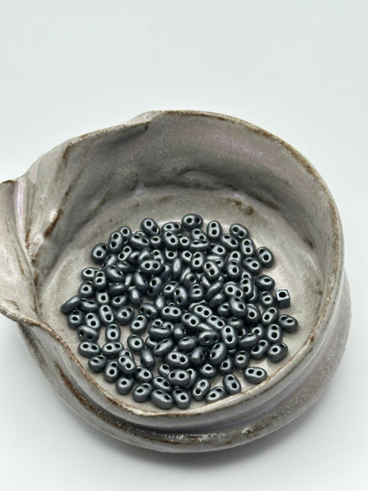Small container filled with black superduo beads on a light gray background