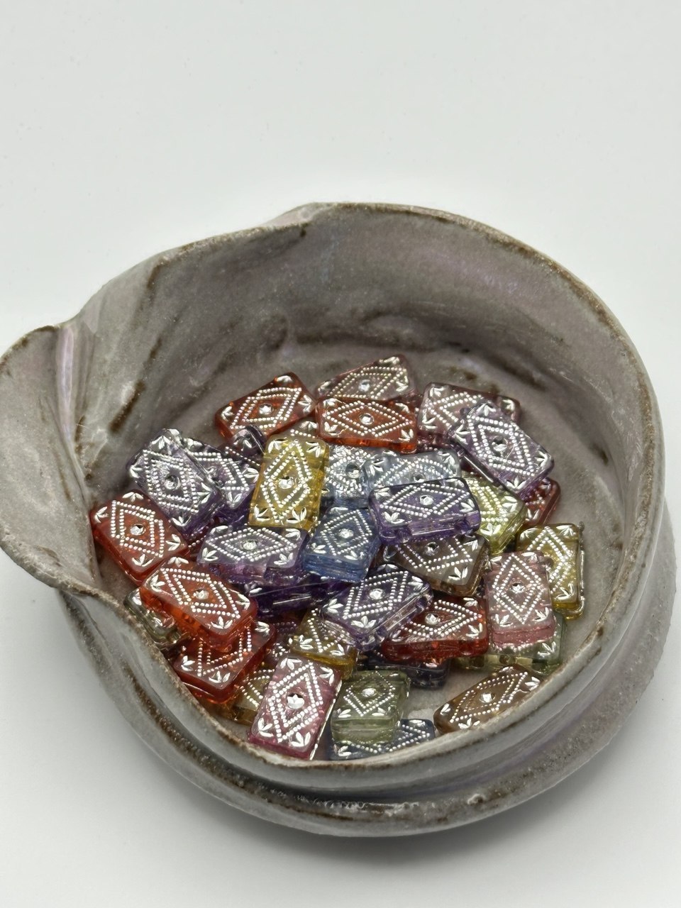 Ceramic bowl with colorful geometric 2-hole beads on a white background