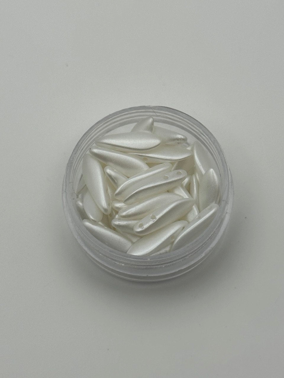 Clear container with white decorative dagger beads on a light gray background
