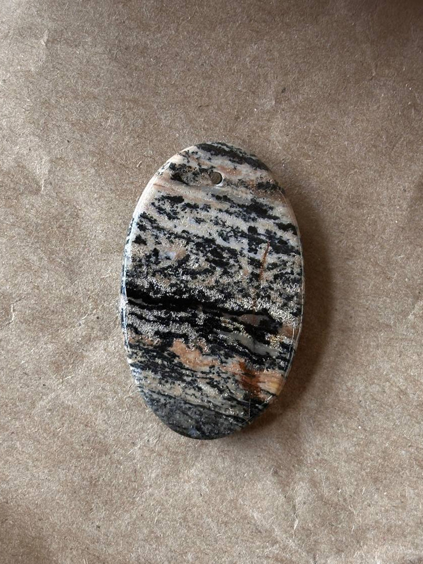 An oval dendritic jasper cabochon on brown paper background