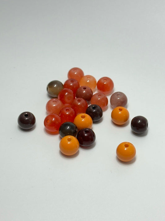A pile of 7mm painted red orange brown round glass beads on white surface