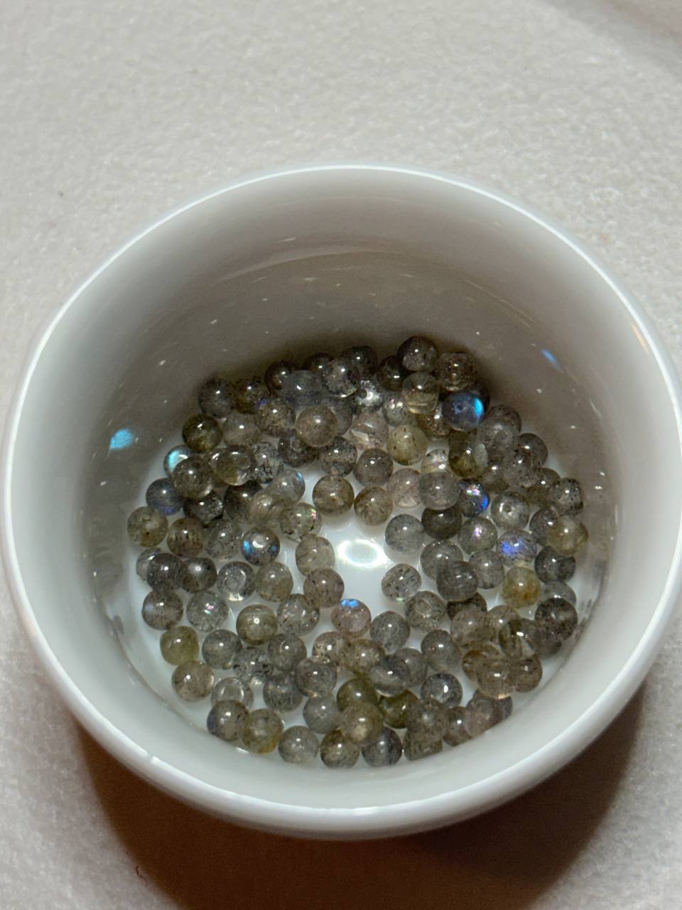 Small white bowl filled with small, round, multicolored beads on a light gray background.