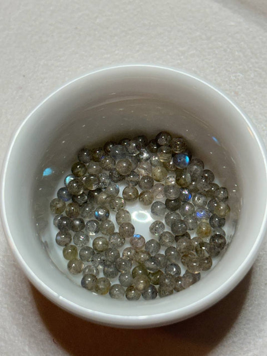 Small white bowl filled with small, round, multicolored beads on a light gray background.