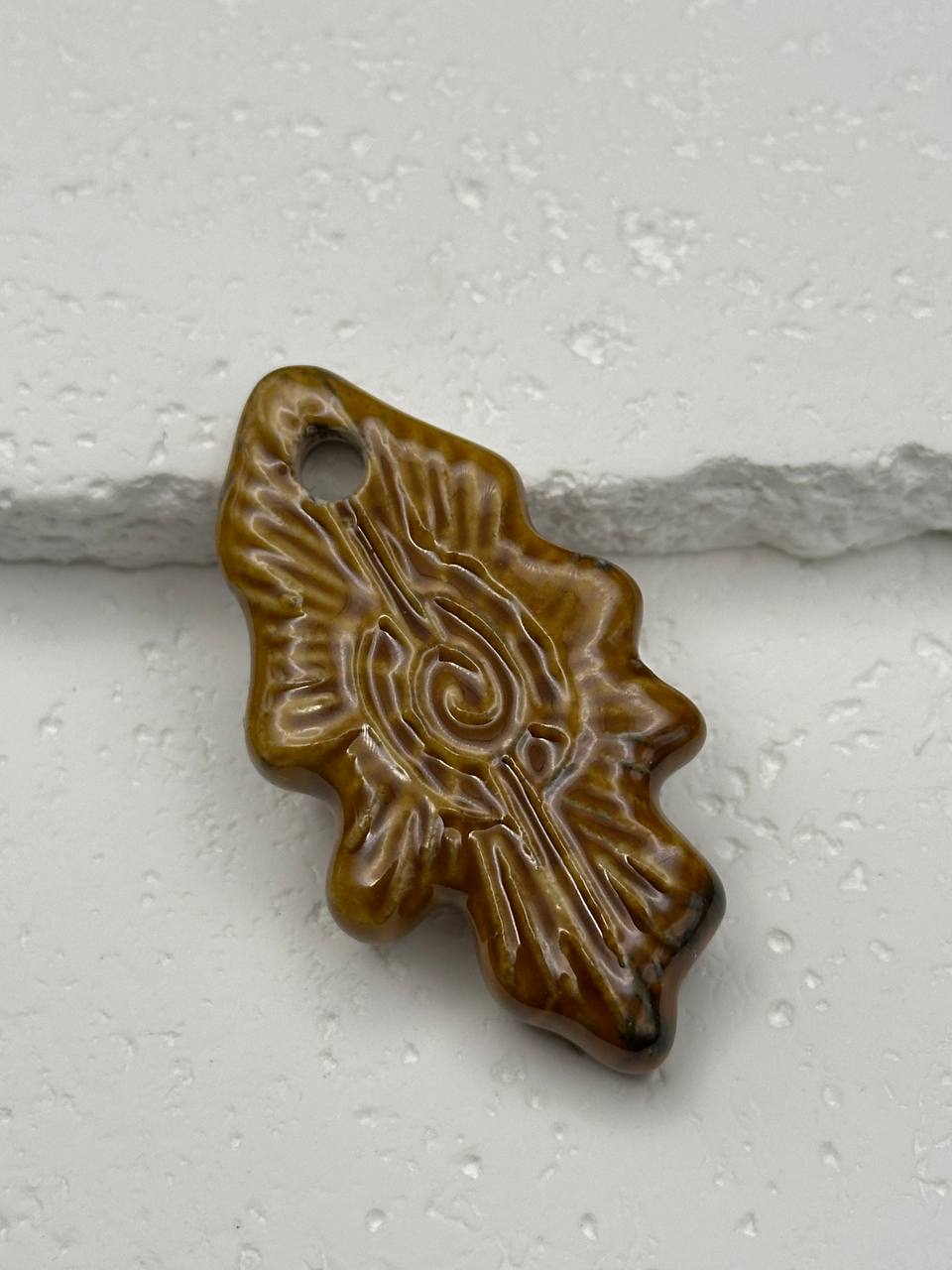 Brown ceramic pendant with intricate design on a white background