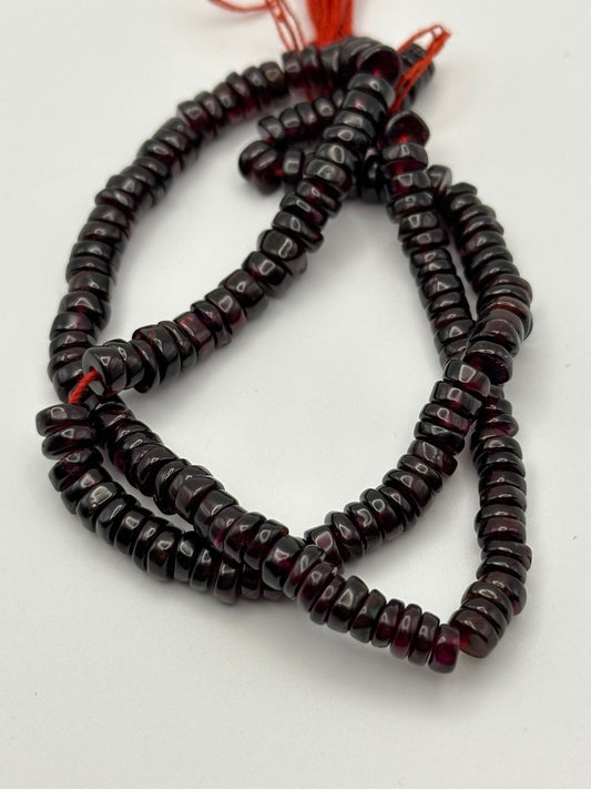 a string of flat rondelle garnet beads on a white surface