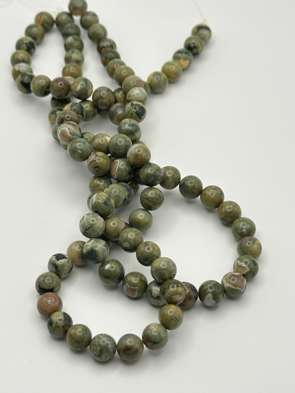 A string of green and brown round smooth rhyolite beads on a white surface