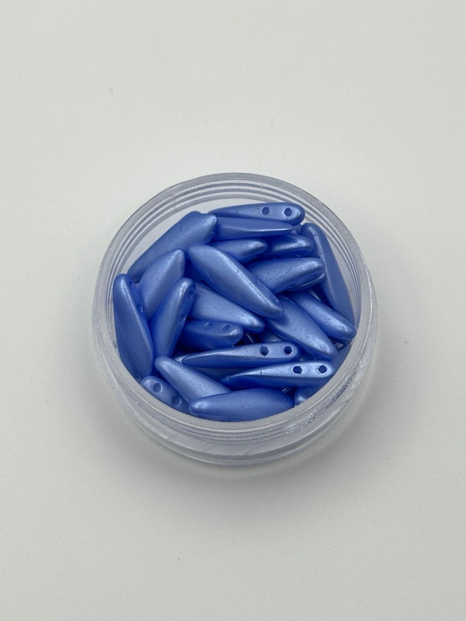 Clear container filled with blue dagger beads on a light gray background