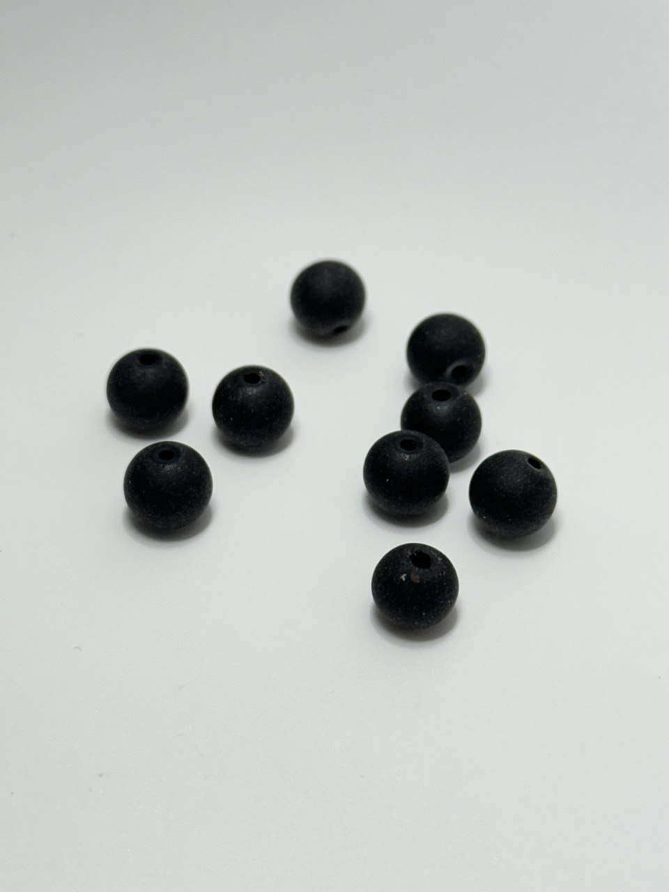 Nine small matte black round beads with pre-drilled holes, scattered on a plain white surface.