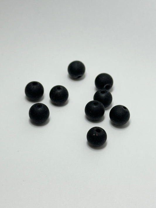 Nine small matte black round beads with pre-drilled holes, scattered on a plain white surface.