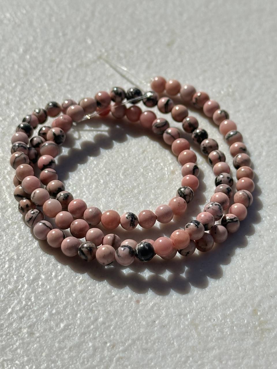 Pink opaque rhodonite with black inclusions on white surface