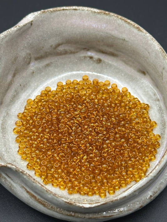 Small container filled with small honey beads on a dark background