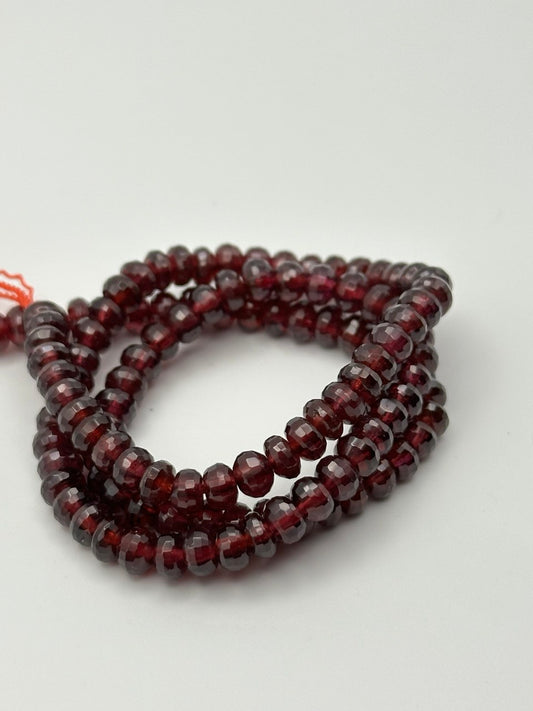 a string of faceted rondelle garnet beads on a white surface