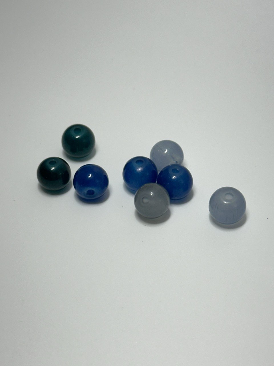 Eight small translucent round beads in assorted colors, including dark teal, bright blue, light blue, and gray, arranged on a plain light background.