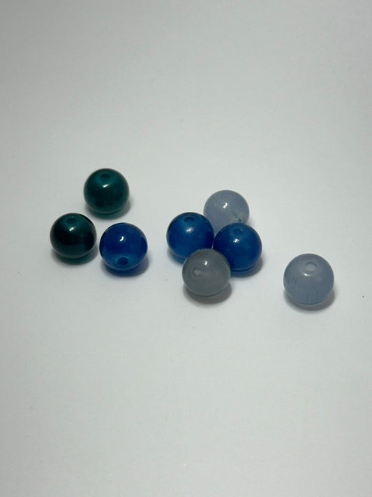 Eight small translucent round beads in assorted colors, including dark teal, bright blue, light blue, and gray, arranged on a plain light background.