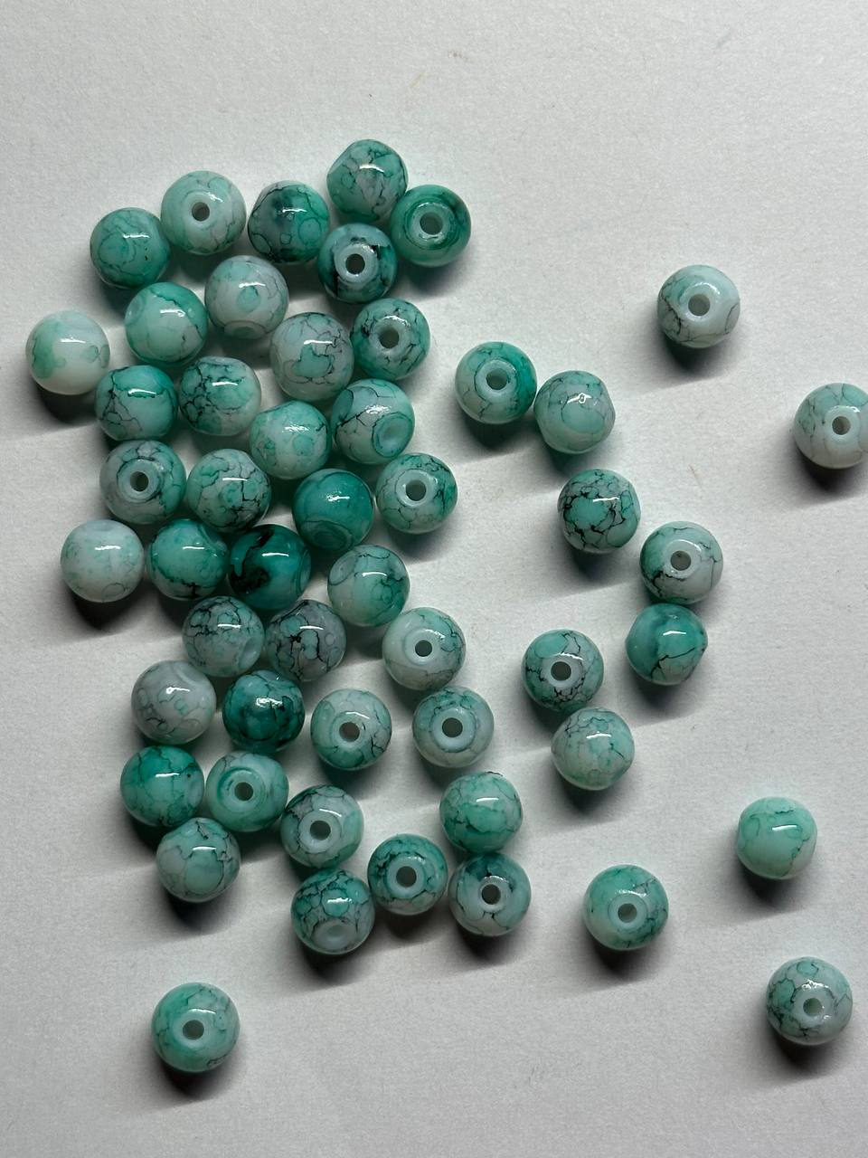Green and white beads scattered on a light gray surface