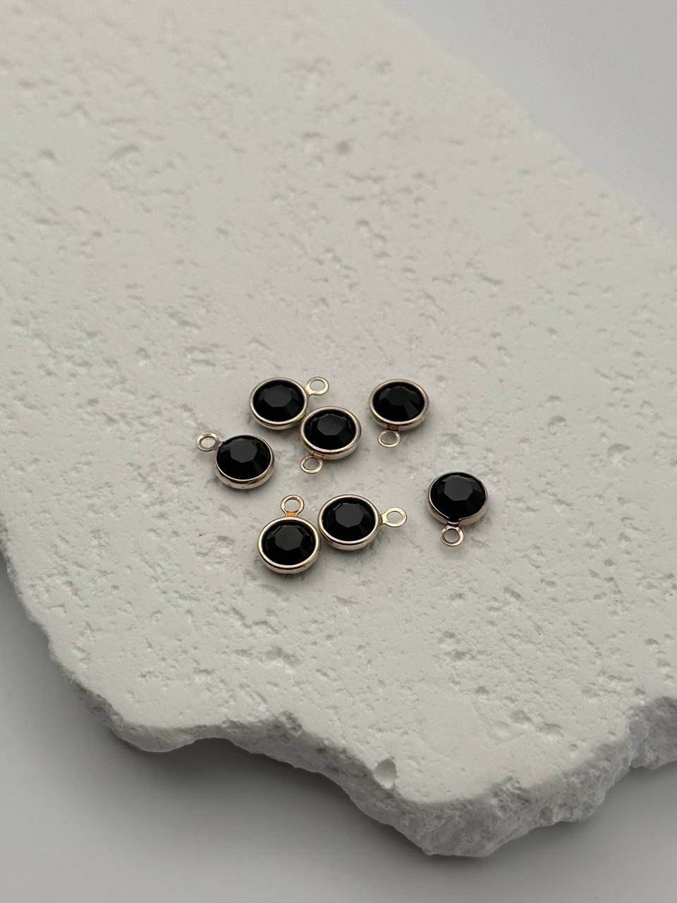 Black gemstone connectors with gold prongs on a textured white surface