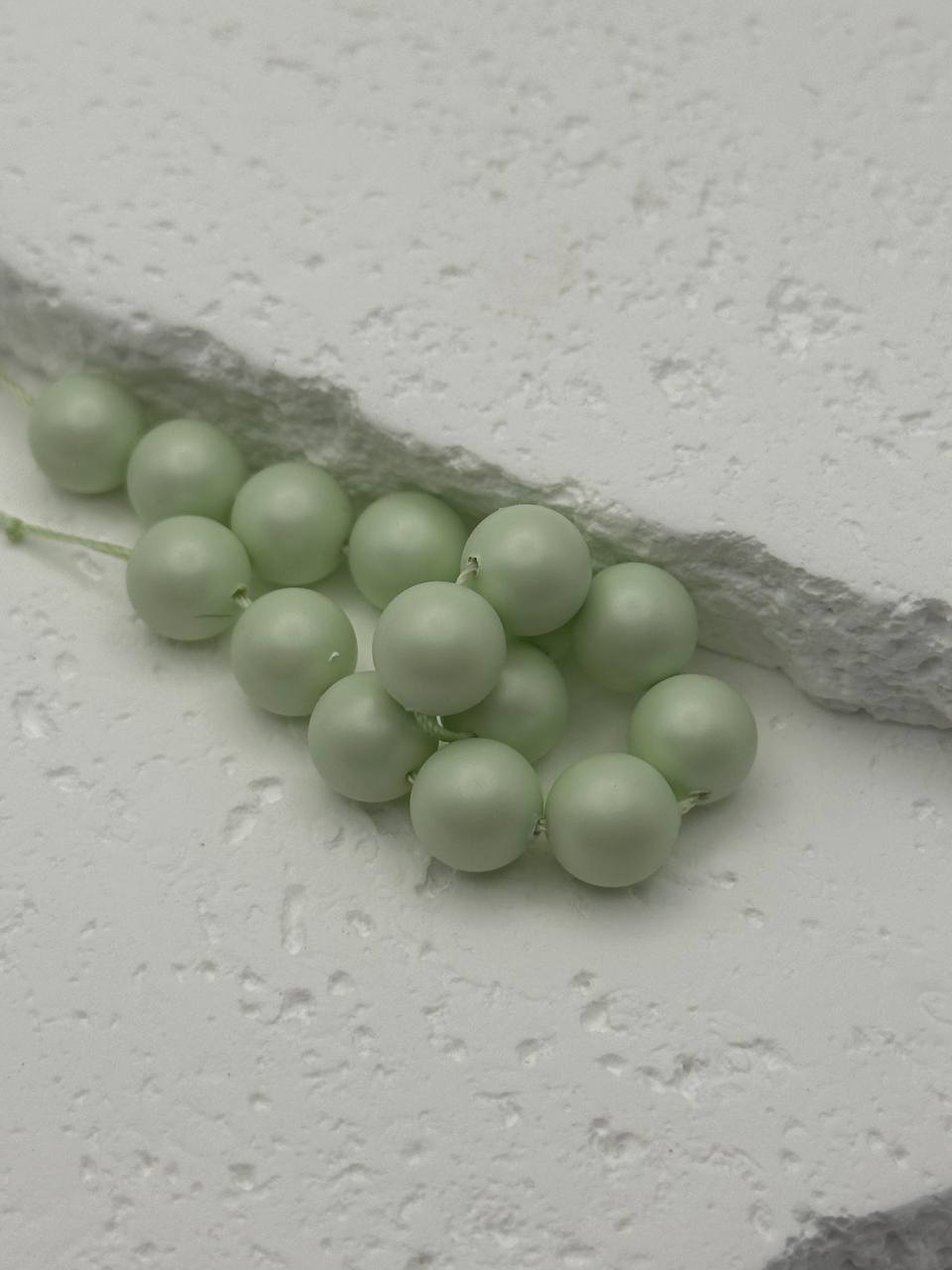 Light green pearls on a textured white surface