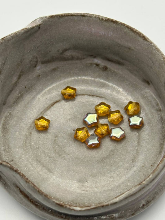 Small amber-colored star shaped beads on a textured gray surface