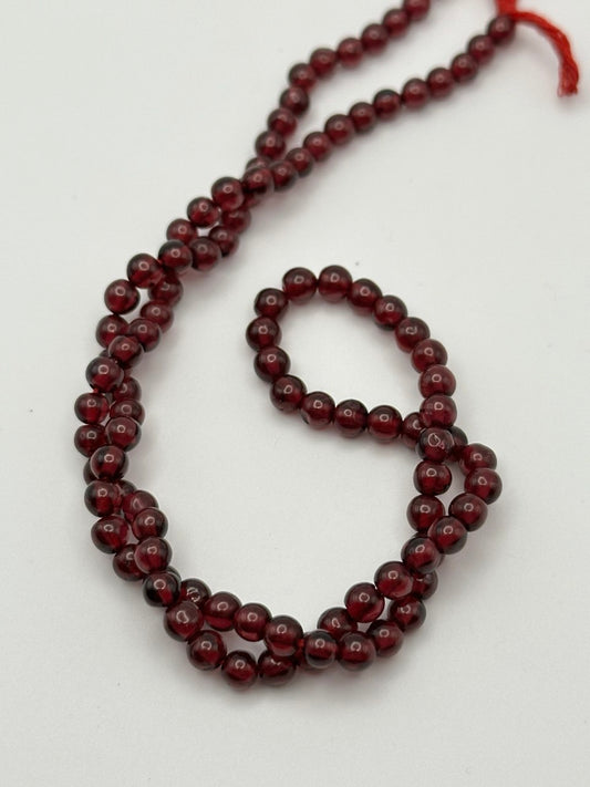 a string of quality red garnet round beads on a white surface