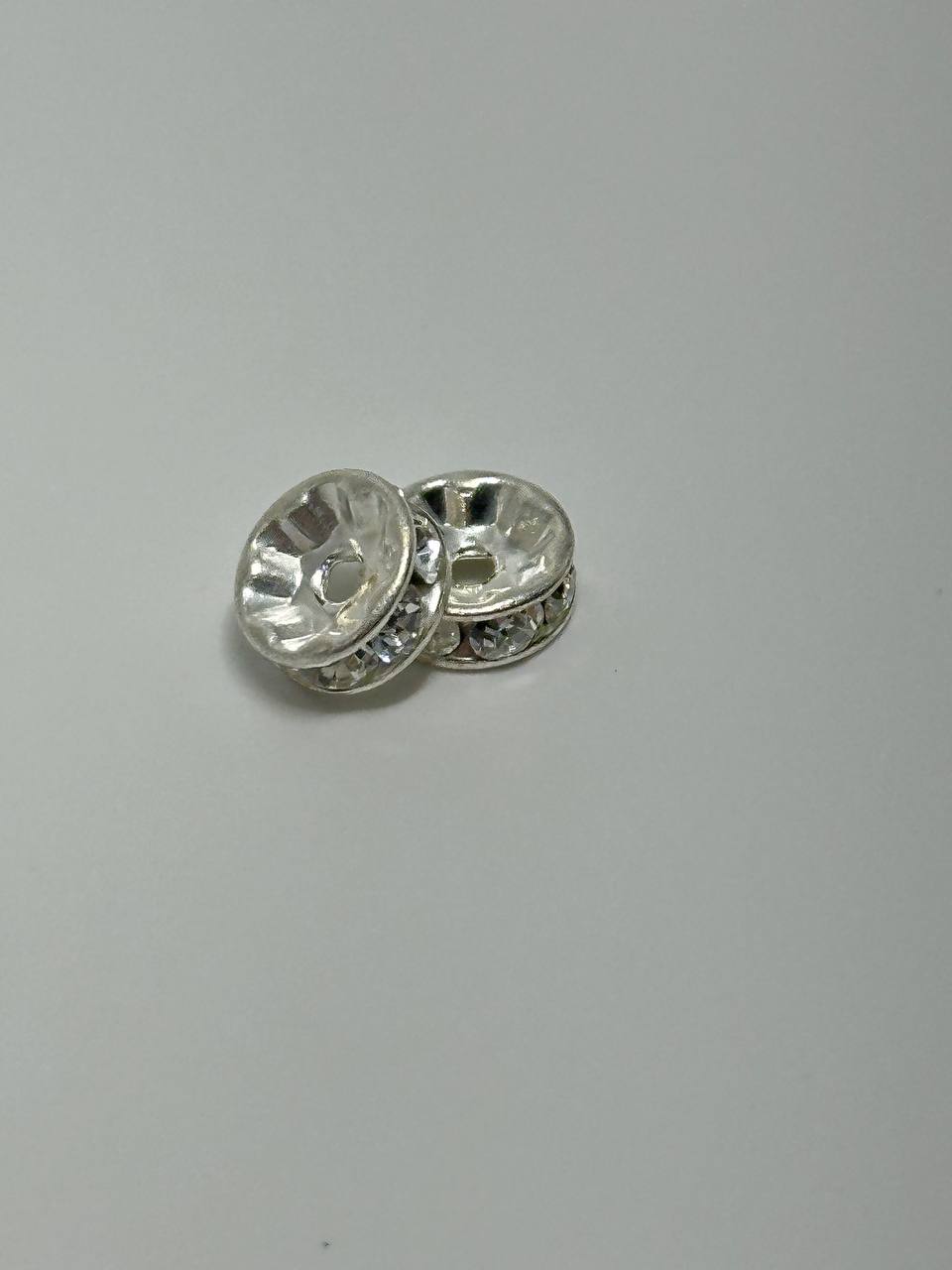 Two silver plated rondelle spacers on white surface
